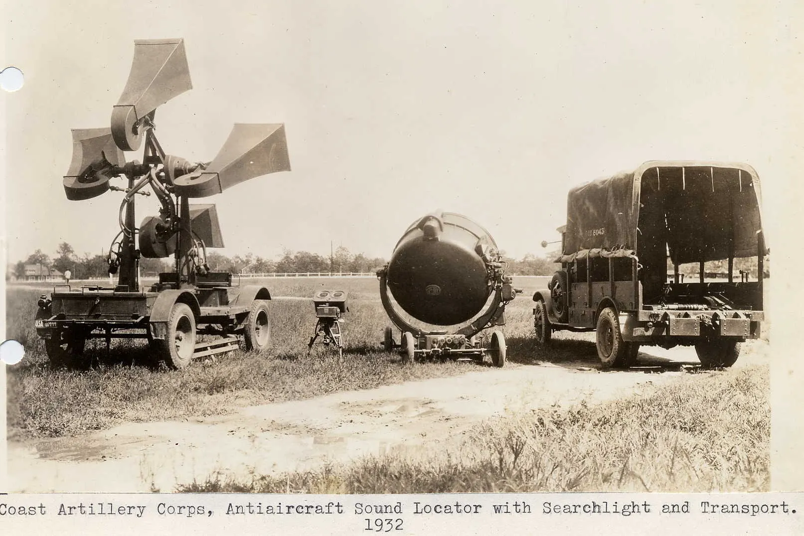 A 1932 U.S. Army sound locator with four large listening horns on a wheeled mount, next to a searchlight and a truck on a grassy field