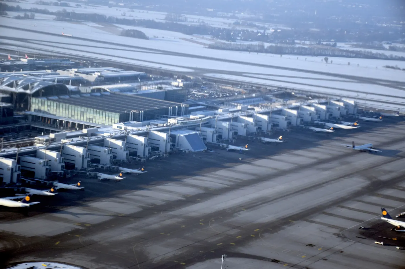 Aerial view of Munich Airport's Terminal 2 and satellite building, with parked aircraft and runways in snow