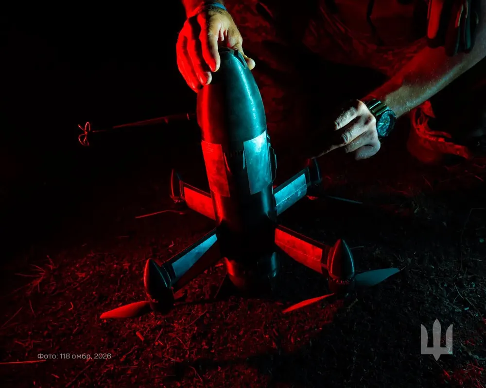 A Ukrainian soldier lit in red light holds a dark bullet-shaped Sting interceptor drone, working on it at night