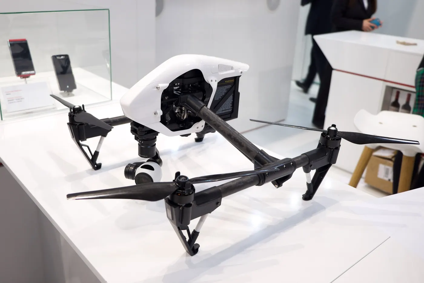 A white DJI Inspire 1 quadcopter with carbon-fibre arms raised and a camera gimbal underneath, on a display table
