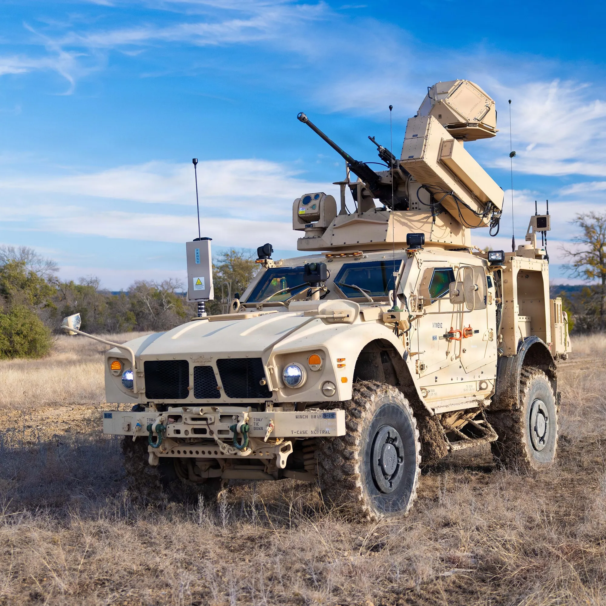 A U.S. Army M-LIDS counter-drone vehicle on dry grass, carrying a 30 mm gun and a box-shaped Ku-band radar on its roof under a blue sky