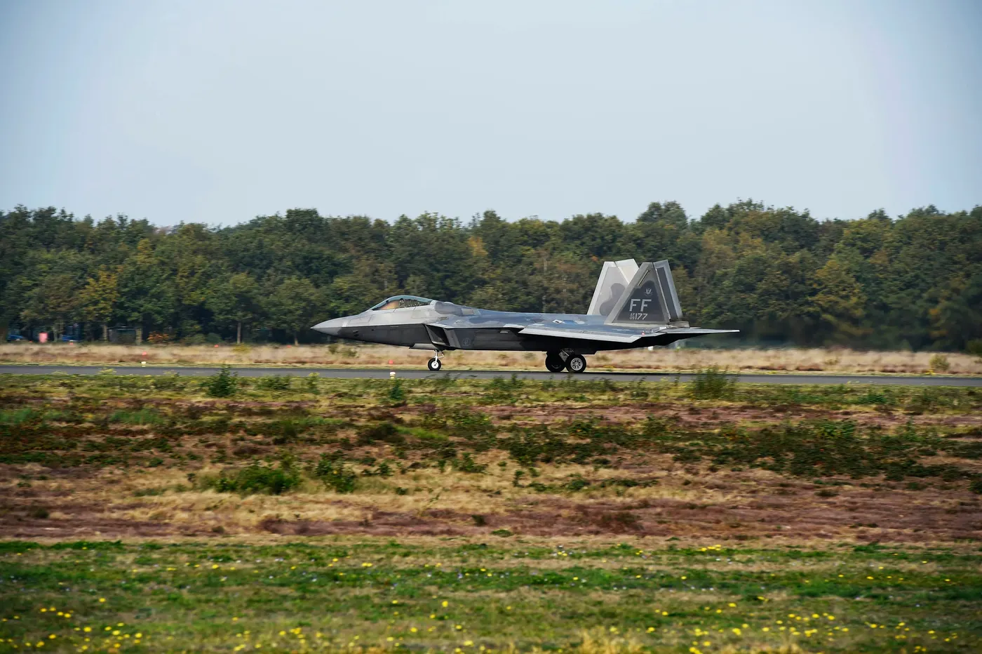 A U.S. Air Force F-22 Raptor taxiing on the runway at Kleine-Brogel Air Base in Belgium, with trees behind