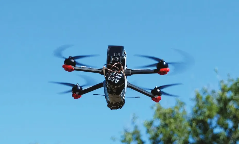 A small FPV quadcopter with red-tipped propellers flying against a blue sky