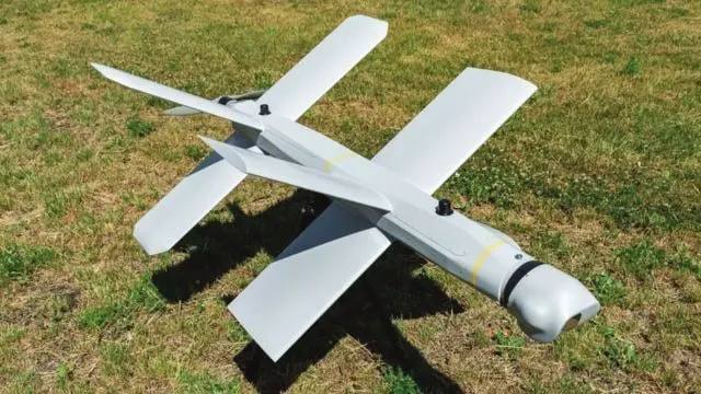 A white Lancet loitering munition with X-shaped wings resting on grass