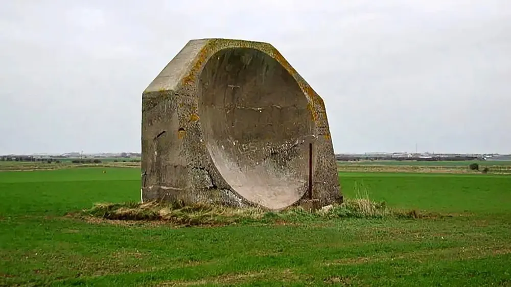 A large disc-shaped concrete acoustic mirror standing alone in a green field at Kilnsea, England