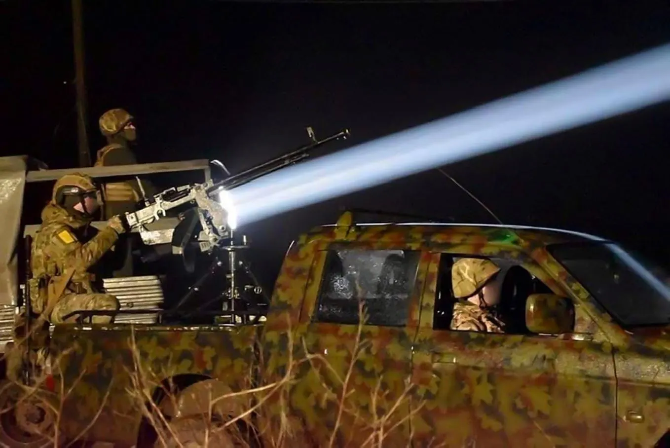 A Ukrainian mobile fire team on a camouflaged pickup truck fires a heavy machine gun into the night sky, its tracer beam lighting the frame