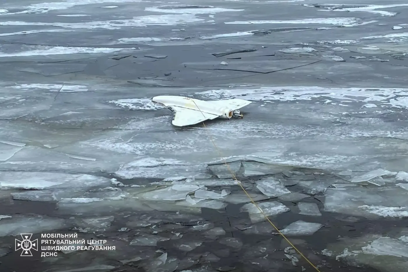 A downed white Gerbera decoy drone, shaped like a Shahed, lying on broken river ice